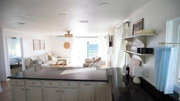 A modern kitchen with a central island, white cabinetry, and a view to a living area with a sofa and a dining table.