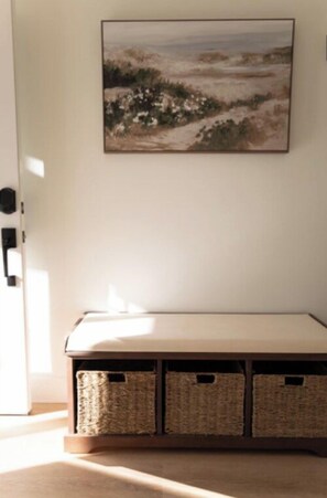 Une pièce avec un banc, un tableau accroché au mur et des paniers placés sous le banc.