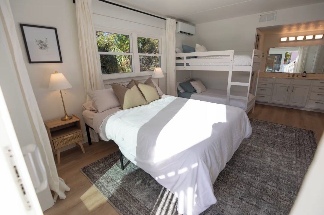 A bedroom with a bed, a bedside table, a lamp, a bunk bed, and a mirror.