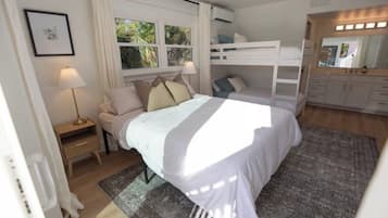 A bedroom with a bed, a bedside table, a lamp, a bunk bed, and a mirror.