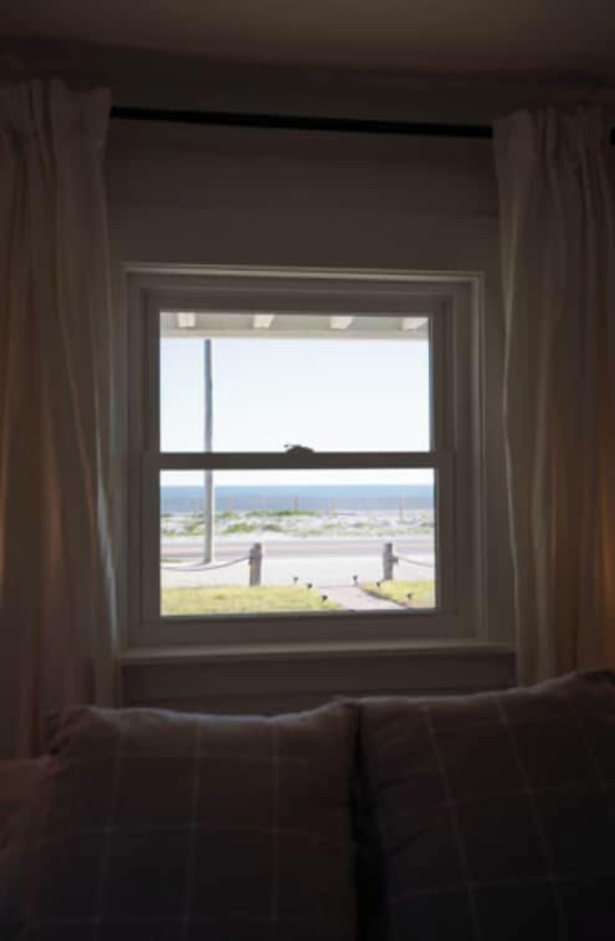Una habitación con ventana que da a una calle, cortinas y una cama con cabecero.