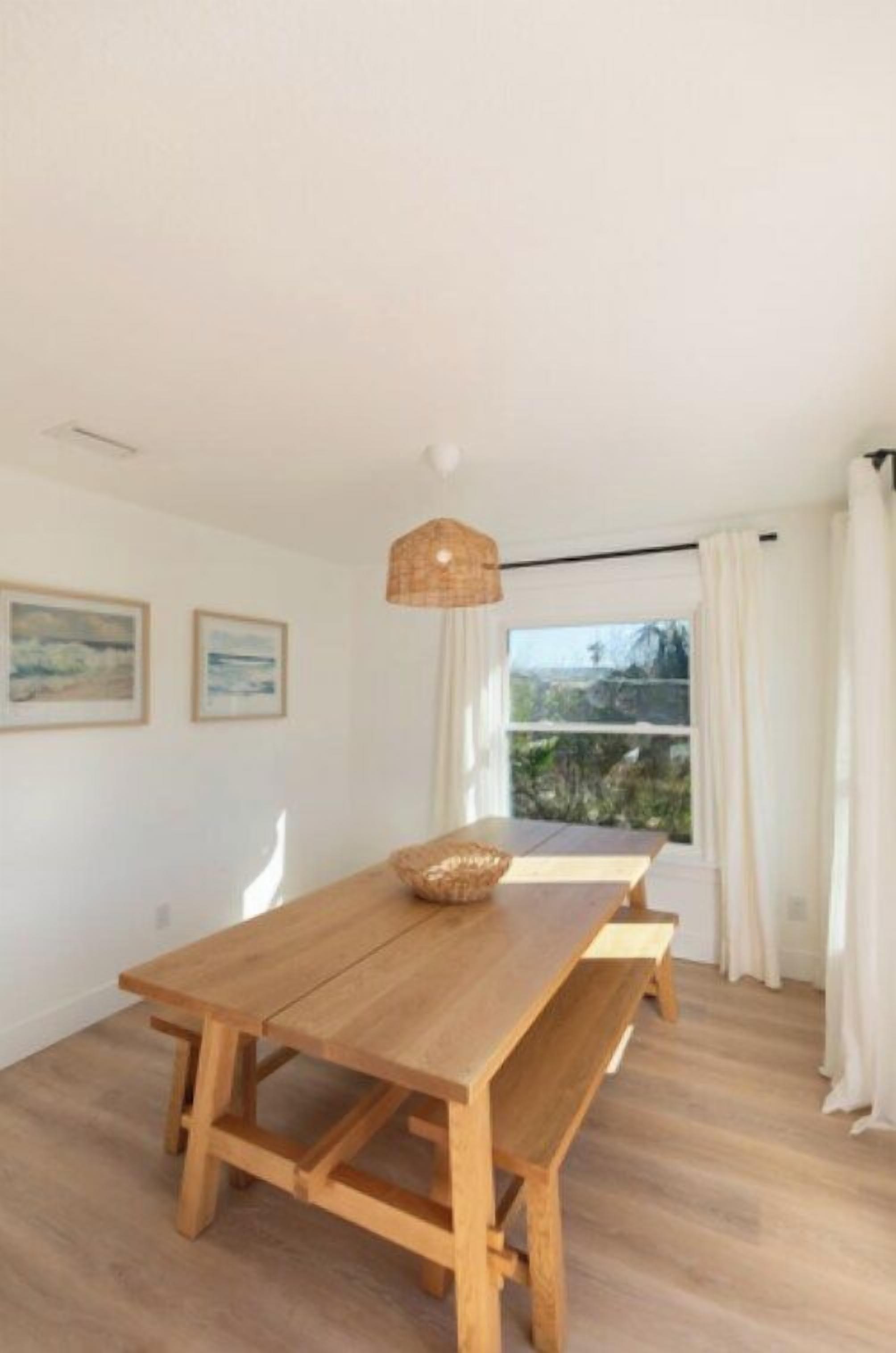 A wooden dining table with benches, a hanging light fixture, and a window with curtains.