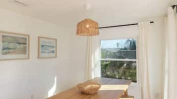 A wooden dining table with benches, a hanging light fixture, and a window with curtains.