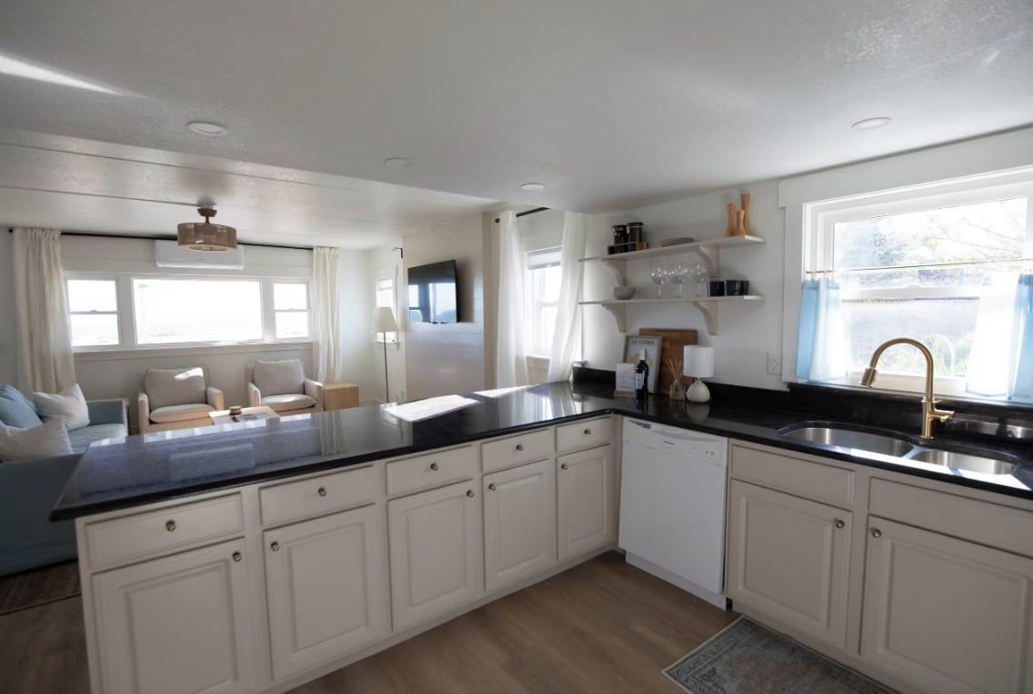 A modern kitchen with white cabinets, a black countertop, and a built-in dishwasher.