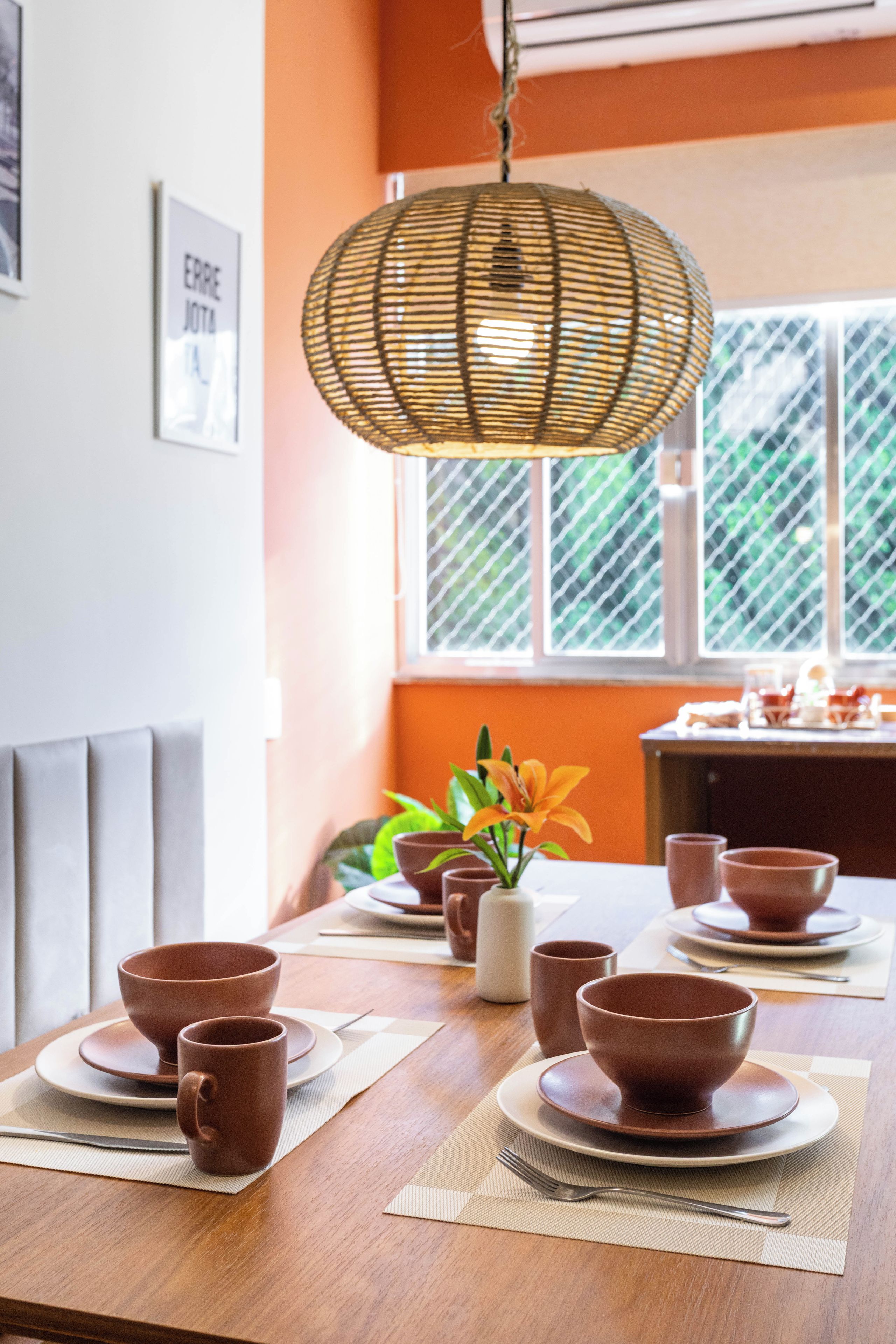 A dining table set with bowls and cups, a hanging light fixture, and a window with a view of greenery.