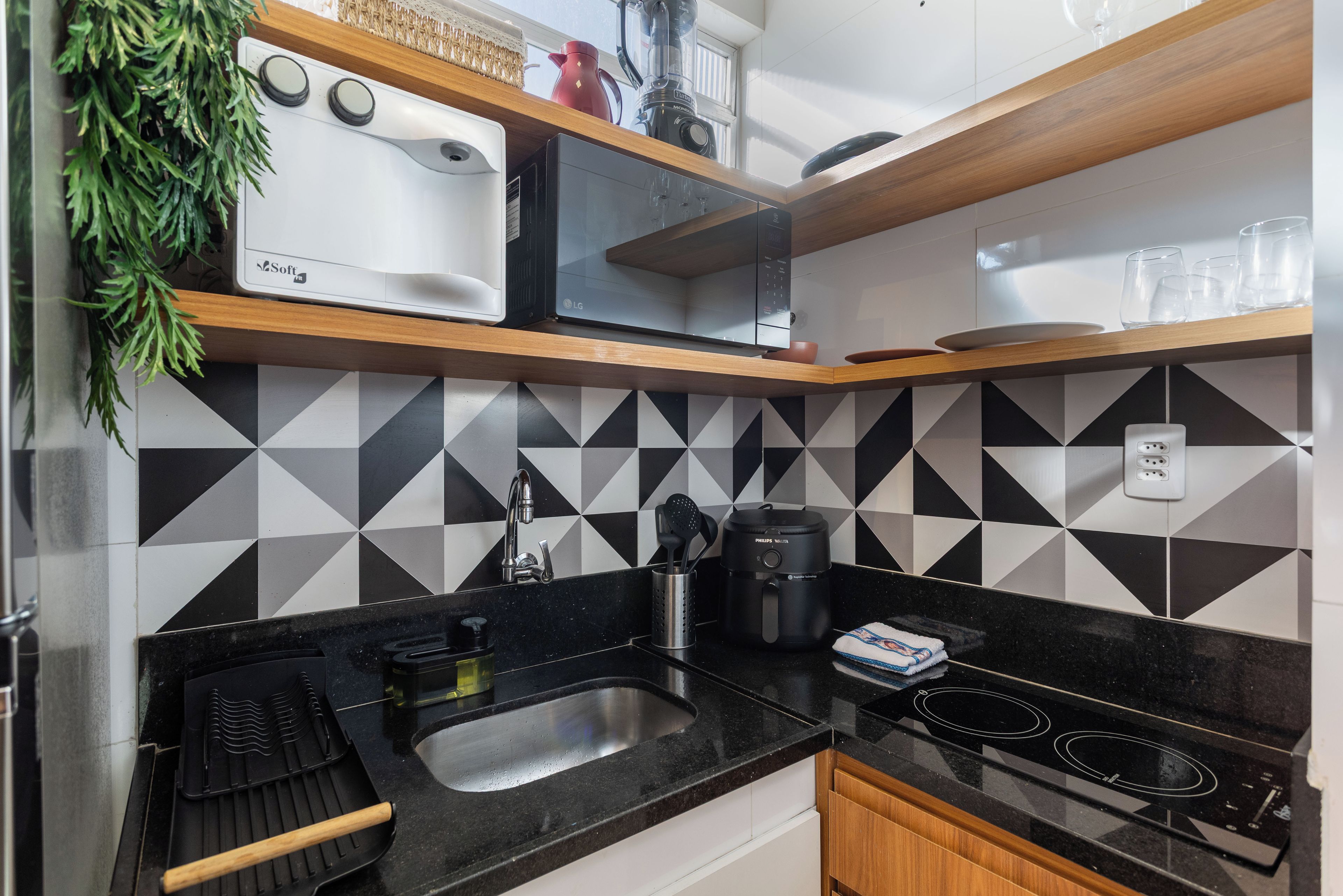 Eine moderne Küche mit weiß-schwarzem geometrischem Rückwandpaneel, einer Edelstahl-Spüle, einem eingebauten Ofen und einer Kaffeemaschine auf der Arbeitsplatte.