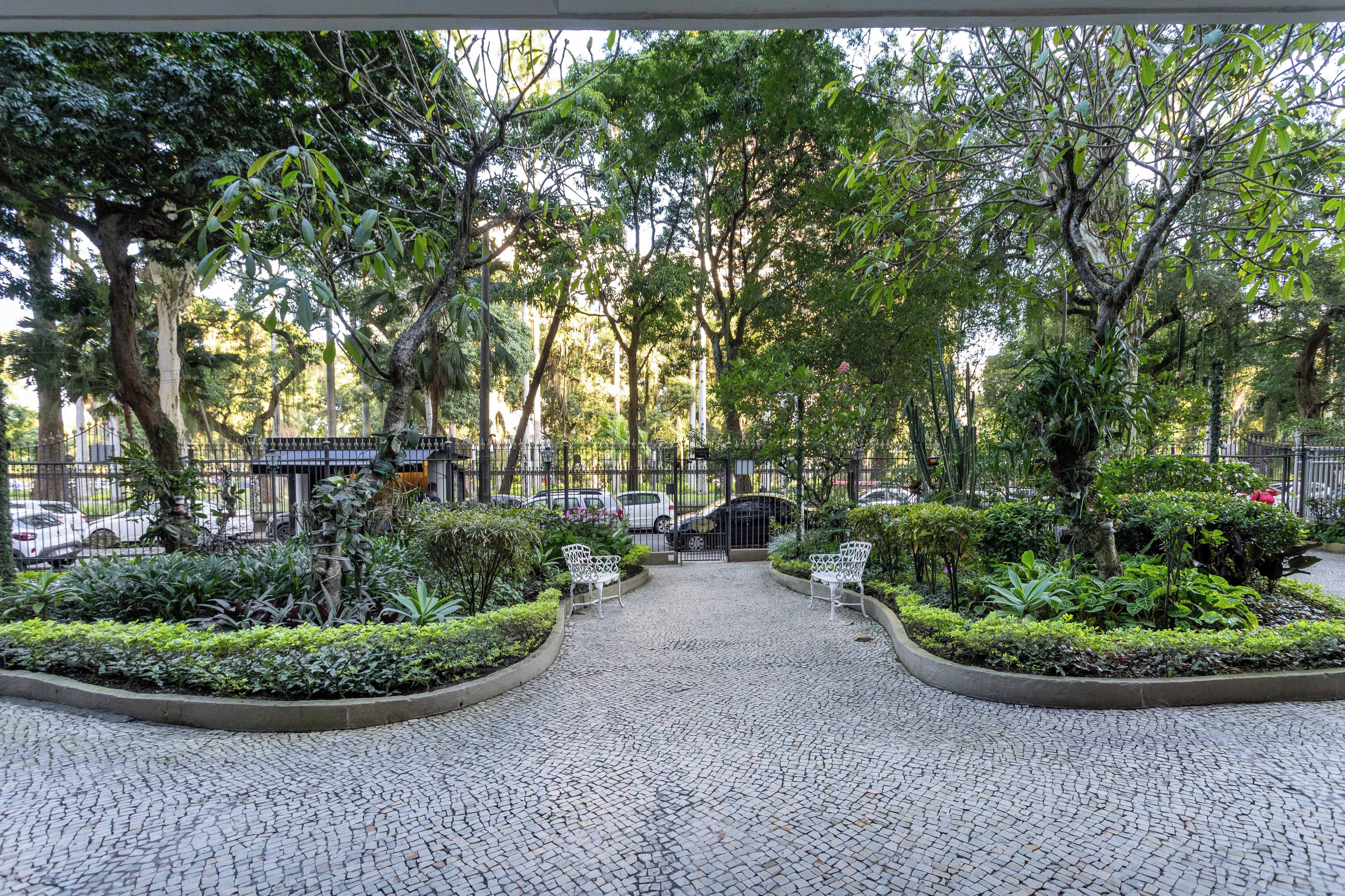 Un chemin pavé traverse un espace aménagé, agrémenté de bancs et d’arbres.