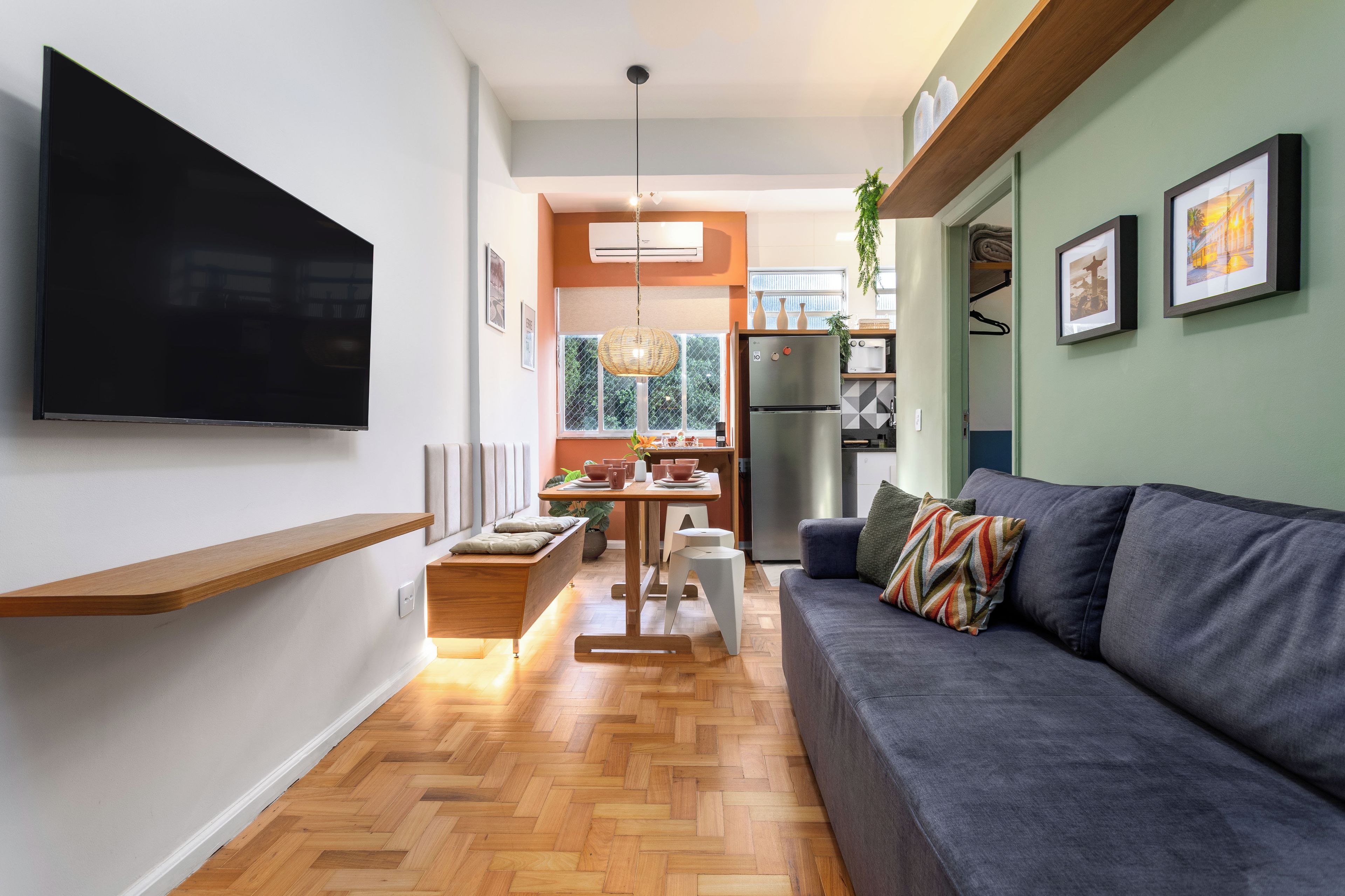 Een moderne woonkamer met een flatscreen televisie, een bank, een eettafel en een keuken met een koelkast.