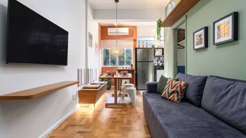 Una sala de estar moderna con televisor de pantalla plana, un sofá, una mesa de comedor y una zona de cocina con refrigerador.