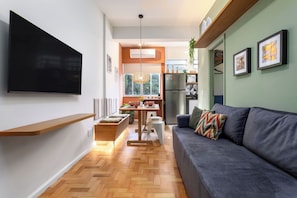 Una sala de estar moderna con televisor de pantalla plana, un sofá, una mesa de comedor y una zona de cocina con refrigerador.