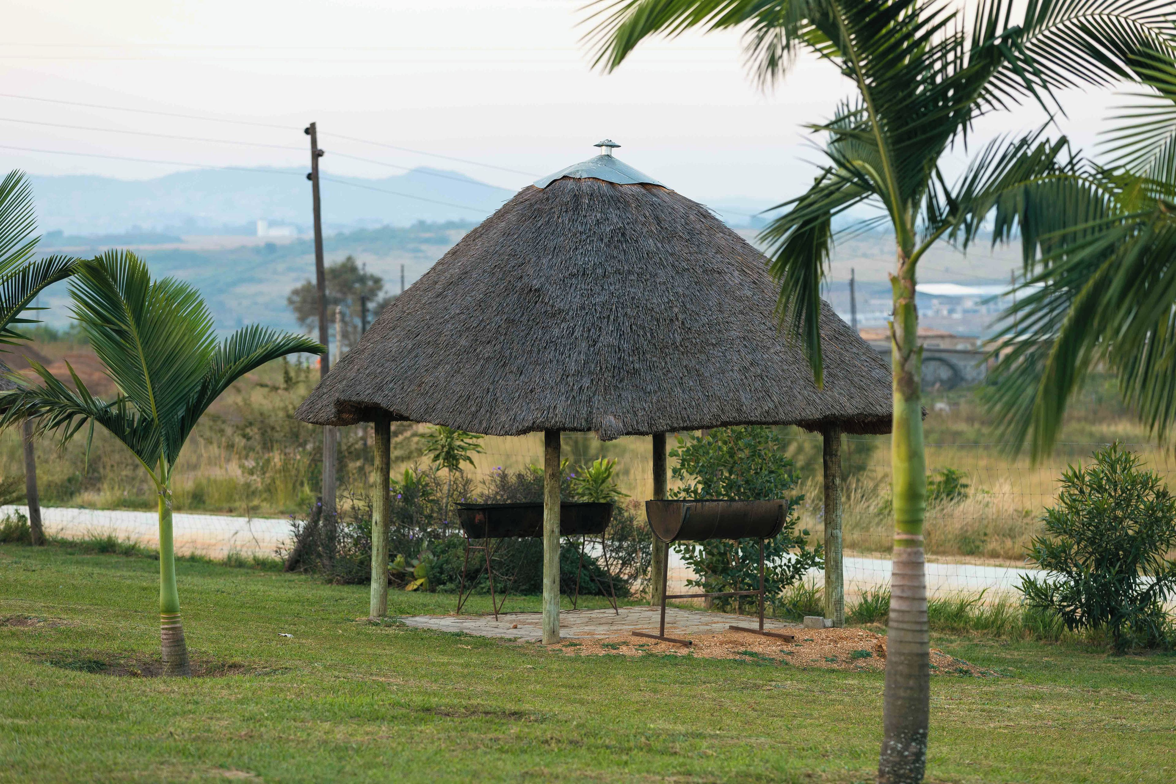 Una estructura de techo de paja con un diseño sencillo, rodeada de vegetación y una vista distante de colinas.
