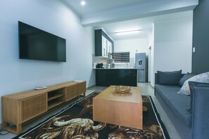 Una sala de estar moderna con un televisor de pantalla plana, una mesa de centro de madera, un sofá y una zona de cocina al fondo.
