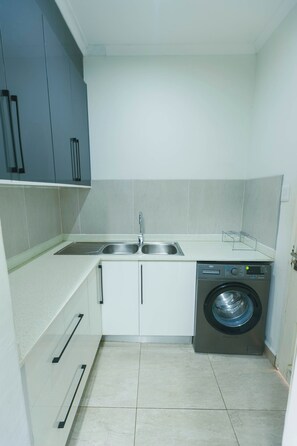 Una cocina compacta con lavadora, un lavamanos doble y una pequeña encimera.
