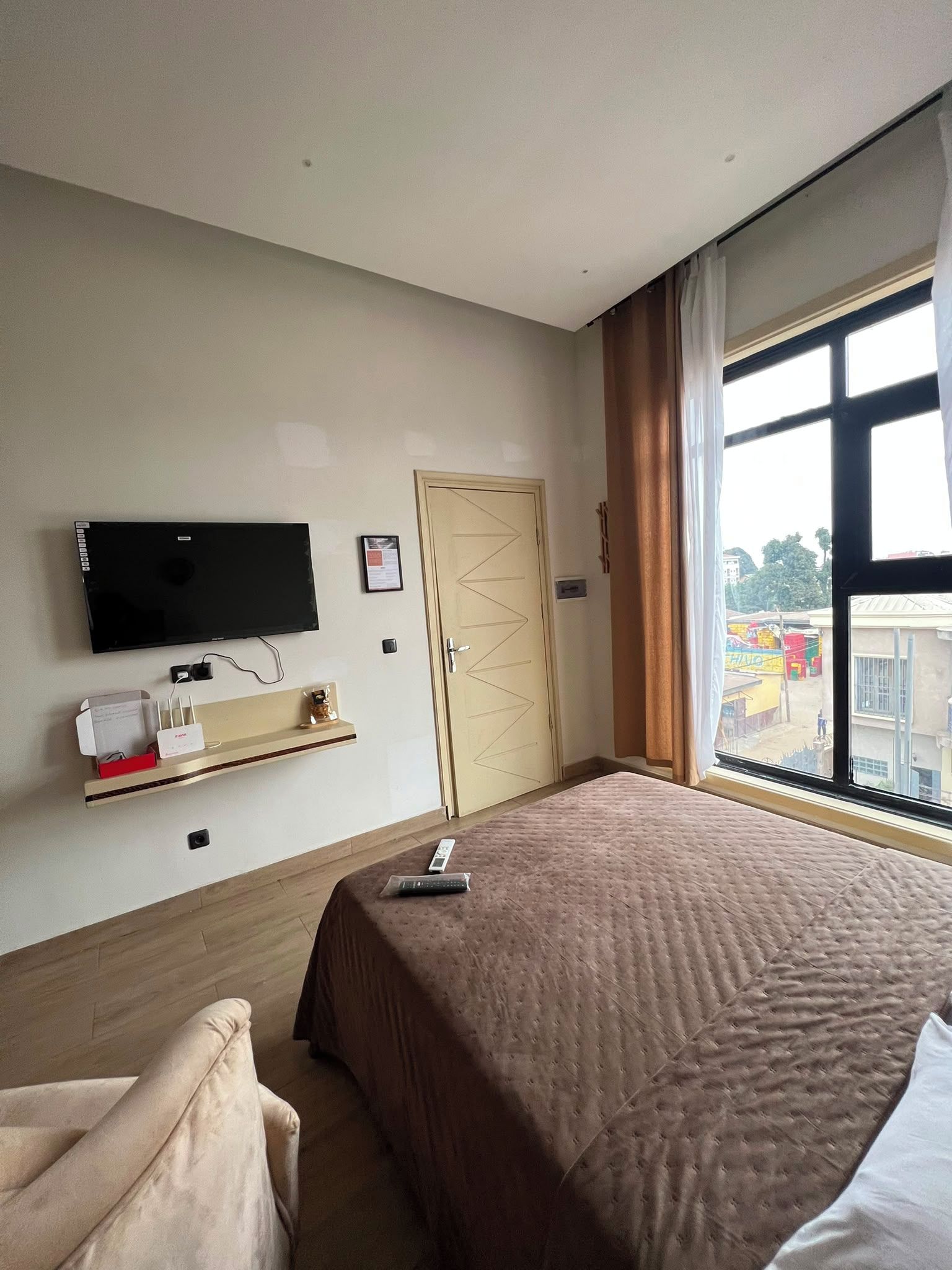 Een hotelkamer met een bed, een aan de muur bevestigde televisie, een deur en een raam met gordijnen.
