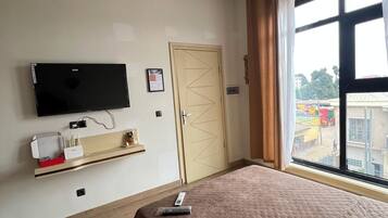 Een hotelkamer met een bed, een aan de muur bevestigde televisie, een deur en een raam met gordijnen.