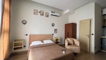 Een hotelkamer met een bed, een stoel, een kledingkast, een bureau en een airconditioning.