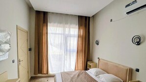Un dormitori amb llit, una nit, un armari i una finestra amb cortines.