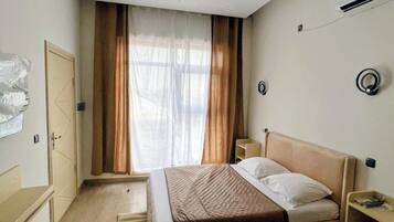 Een slaapkamer met een bed, een nachtkastje, een kledingkast en een raam met gordijnen.