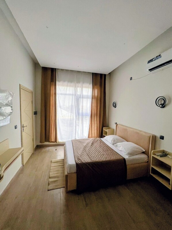A bedroom with a bed, a nightstand, a wardrobe, and a window with curtains.