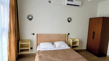 A hotel room with a bed, an air conditioning unit, a wardrobe, and a nightstand.
