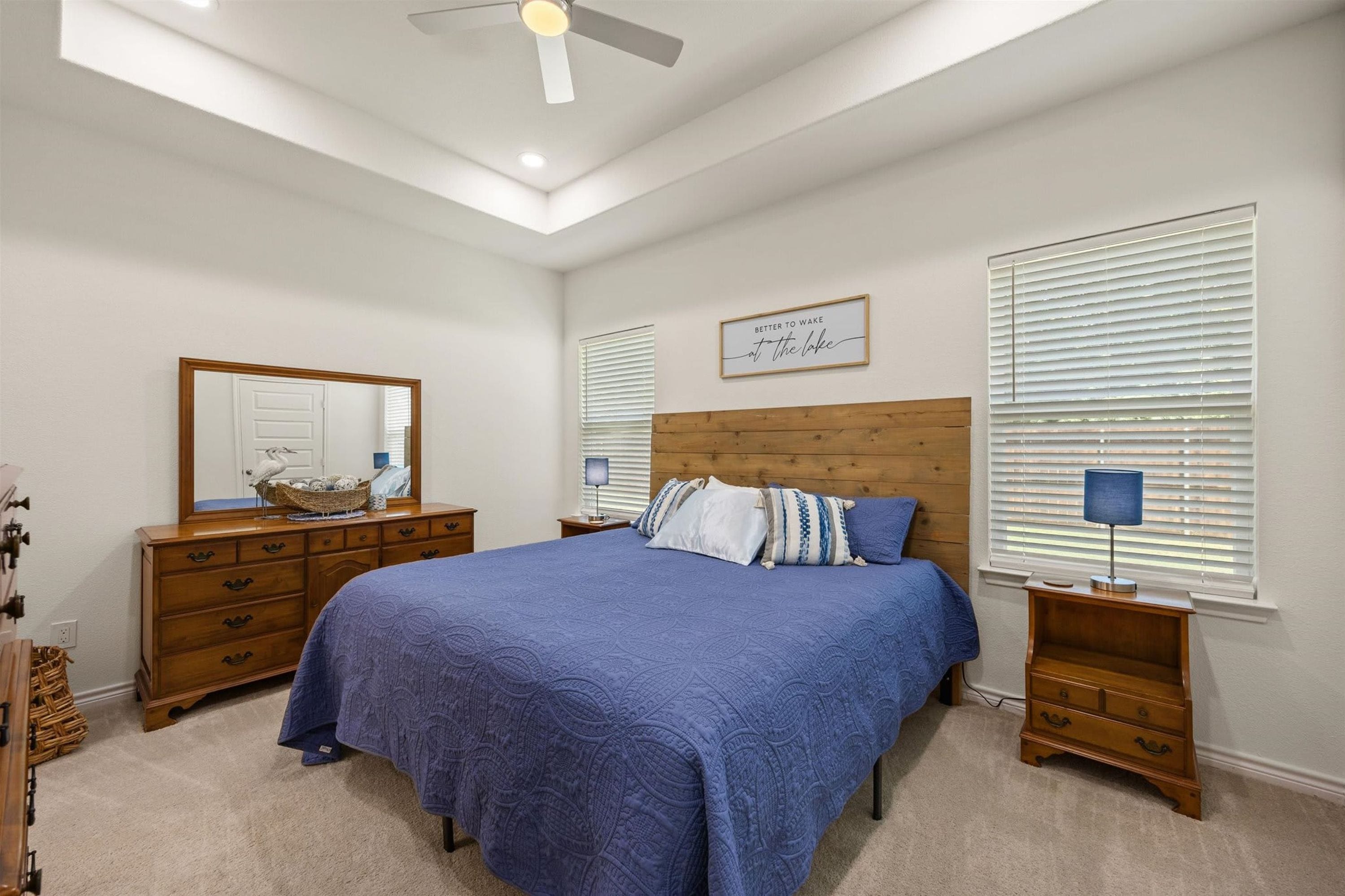 A bedroom with a large bed, wooden headboard, a dresser, a mirror, and a ceiling fan.