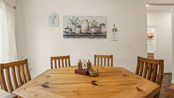 A dining area with a wooden table, four chairs, and a painting of potted plants on the wall.