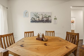 A dining area with a wooden table, four chairs, and a painting of potted plants on the wall. - Wake Up on Lakeside Trail - Sleeps 8 Fire Pit (Granbury)