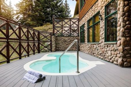 A hot tub on a wooden deck with a stone wall and a wooden fence.