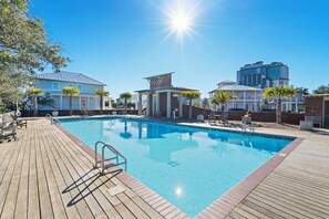 A swimming pool with a wooden deck, surrounded by buildings and palm trees. - Grace Shores Cottage at Tannin by Liquid Life (Orange Beach)