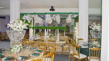 Un salón de banquetes con mesas redondas, sillas doradas y centros de mesa con flores.
