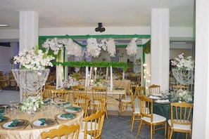 Un salón de banquetes con mesas redondas, sillas doradas y centros de mesa con flores.