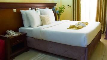 Habitación de hotel con cama, teléfono, mesita de noche y ventana con cortinas.