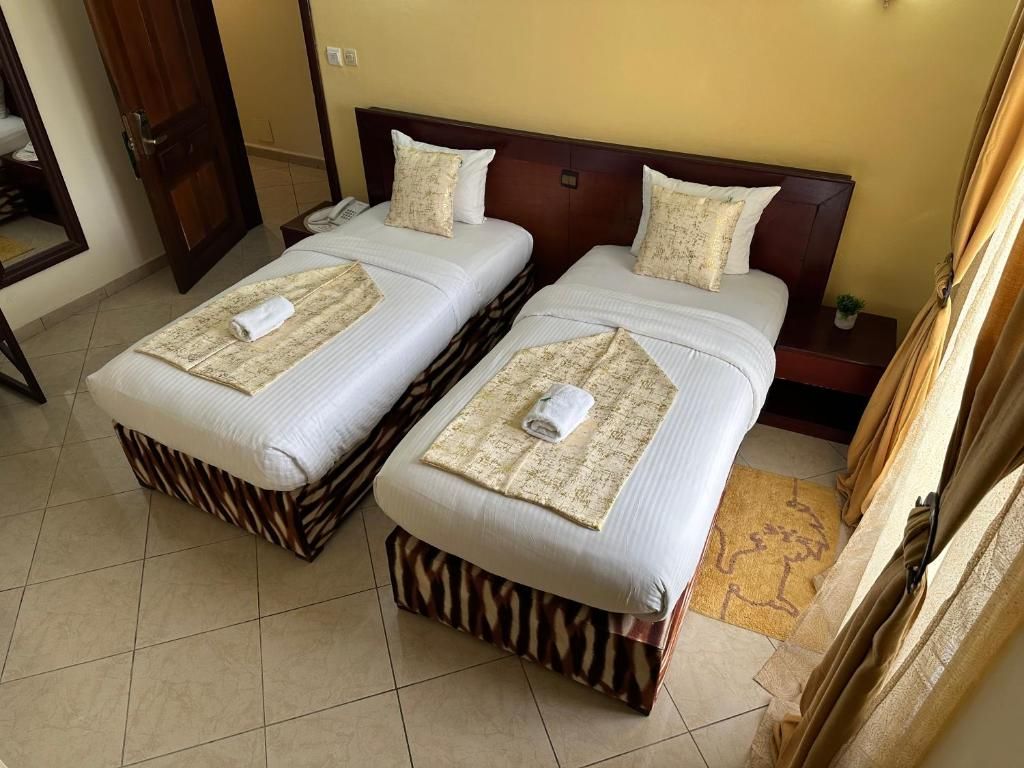 Habitación de hotel con dos camas, un cabecero de madera, una mesita de noche pequeña con una lámpara y un baño visible a través de una puerta abierta.