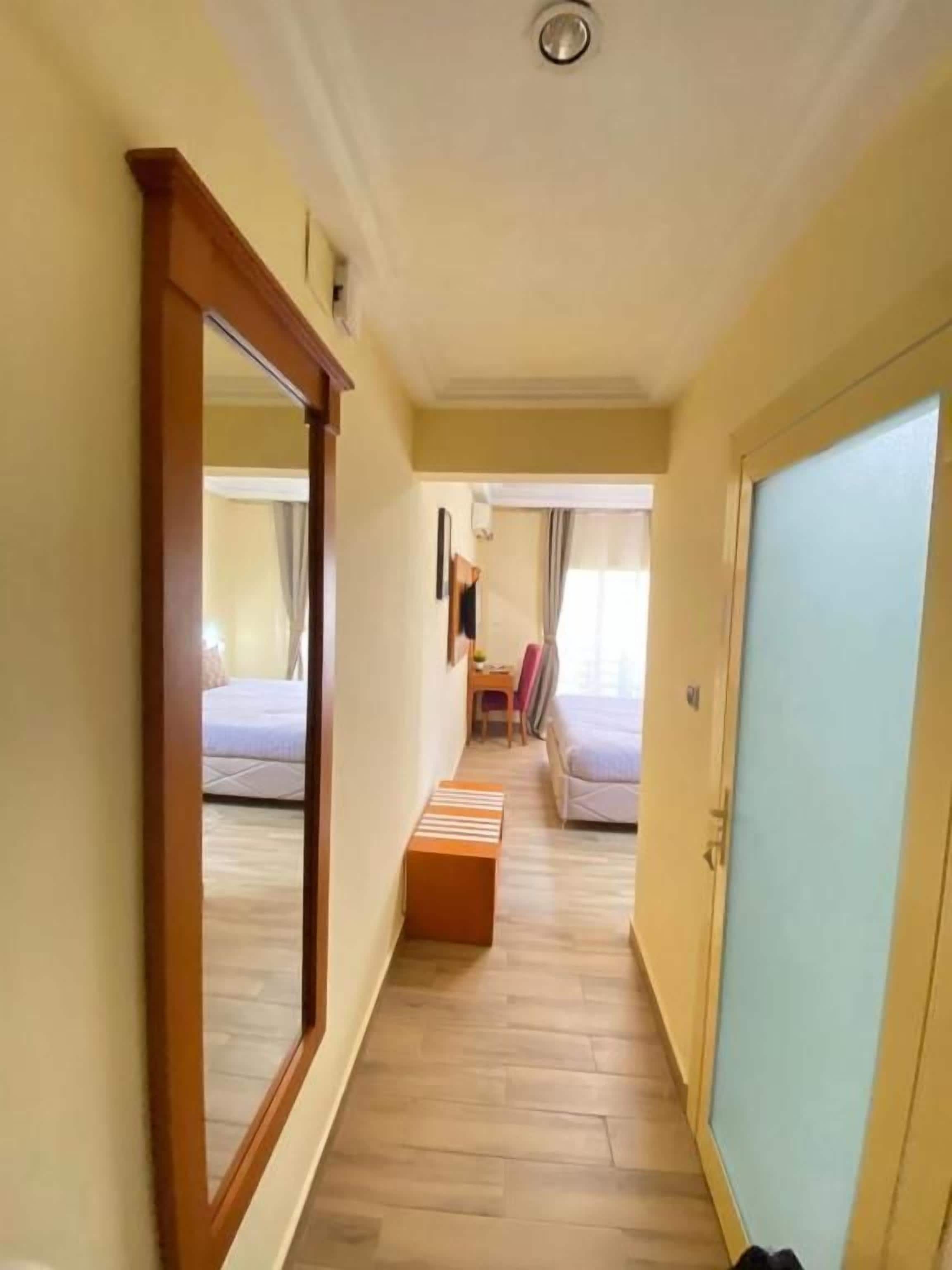 Un corridoio stretto con pavimento in legno, uno specchio a sinistra e un letto con testiera blu in fondo.