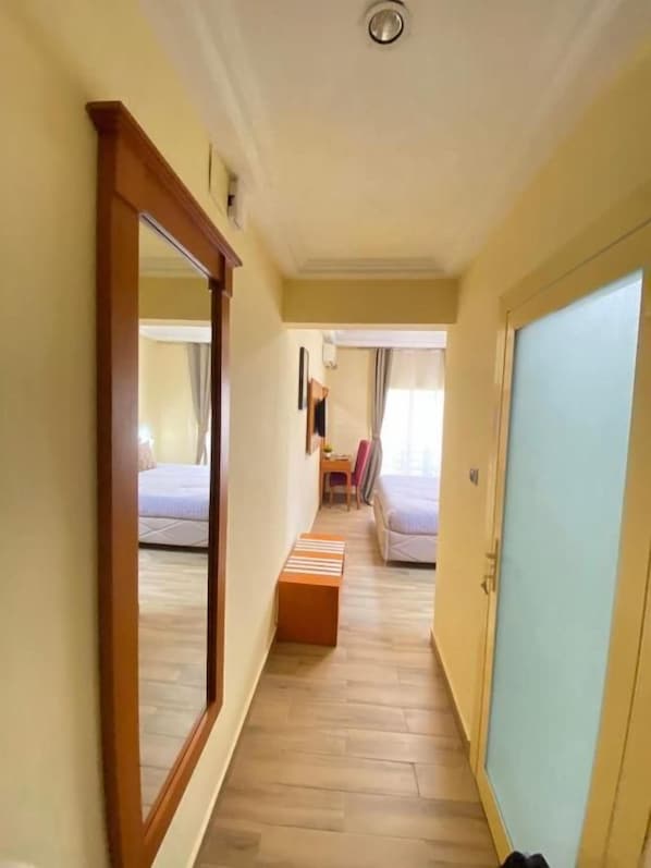 Un pasillo estrecho con suelo de madera, un espejo a la izquierda y una cama con cabecera azul al final.