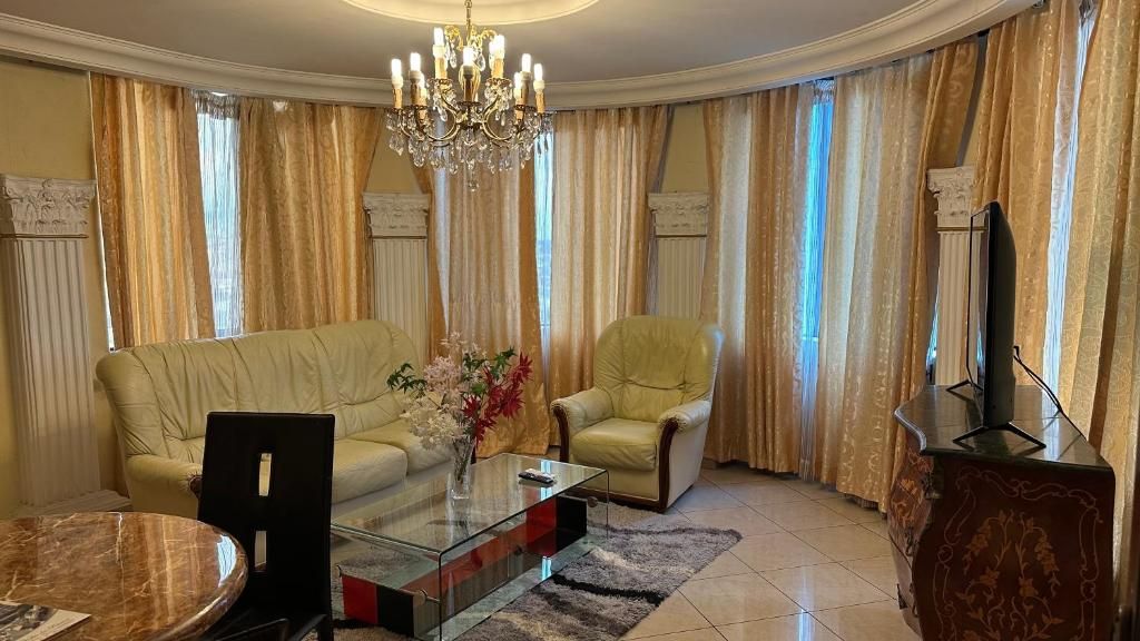 Una sala de estar con sofá, sillón, mesa de centro de vidrio y televisor sobre un mueble.