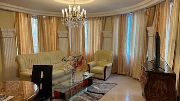 Una sala de estar con sofá, sillón, mesa de centro de vidrio y televisor sobre un mueble.