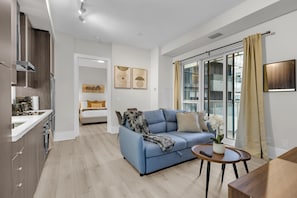 Un appartement moderne comprenant une cuisine, un espace de vie avec un canapé et une table basse, ainsi qu’une grande porte-fenêtre coulissante donnant sur le balcon.