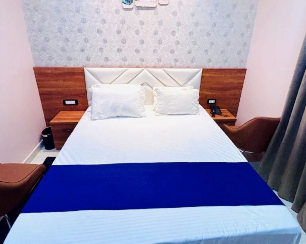 A hotel room with a bed, two pillows, a nightstand with a phone, and a brown chair.
