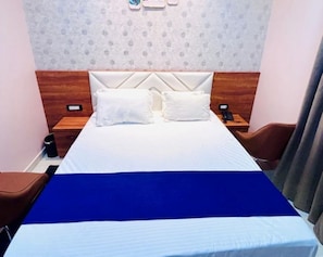 A hotel room with a bed, two pillows, a nightstand with a phone, and a wall with a patterned design. - HOTEL SHREE KARNI PALACE (Sultanpur)