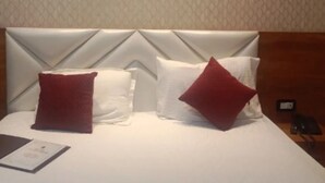 A hotel room with a bed, two pillows, a bedside table, and a nightstand. - HOTEL SHREE KARNI PALACE (Sultanpur)