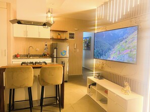 A modern kitchen with a built-in refrigerator, a dining area with two bar stools, and a large flat-screen TV mounted on the wall. - Apartment in the Colonial District (Santo Domingo)
