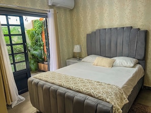 A bedroom with a bed, a nightstand, a lamp, and a view of greenery outside. - Apartment in the Colonial District (Santo Domingo)