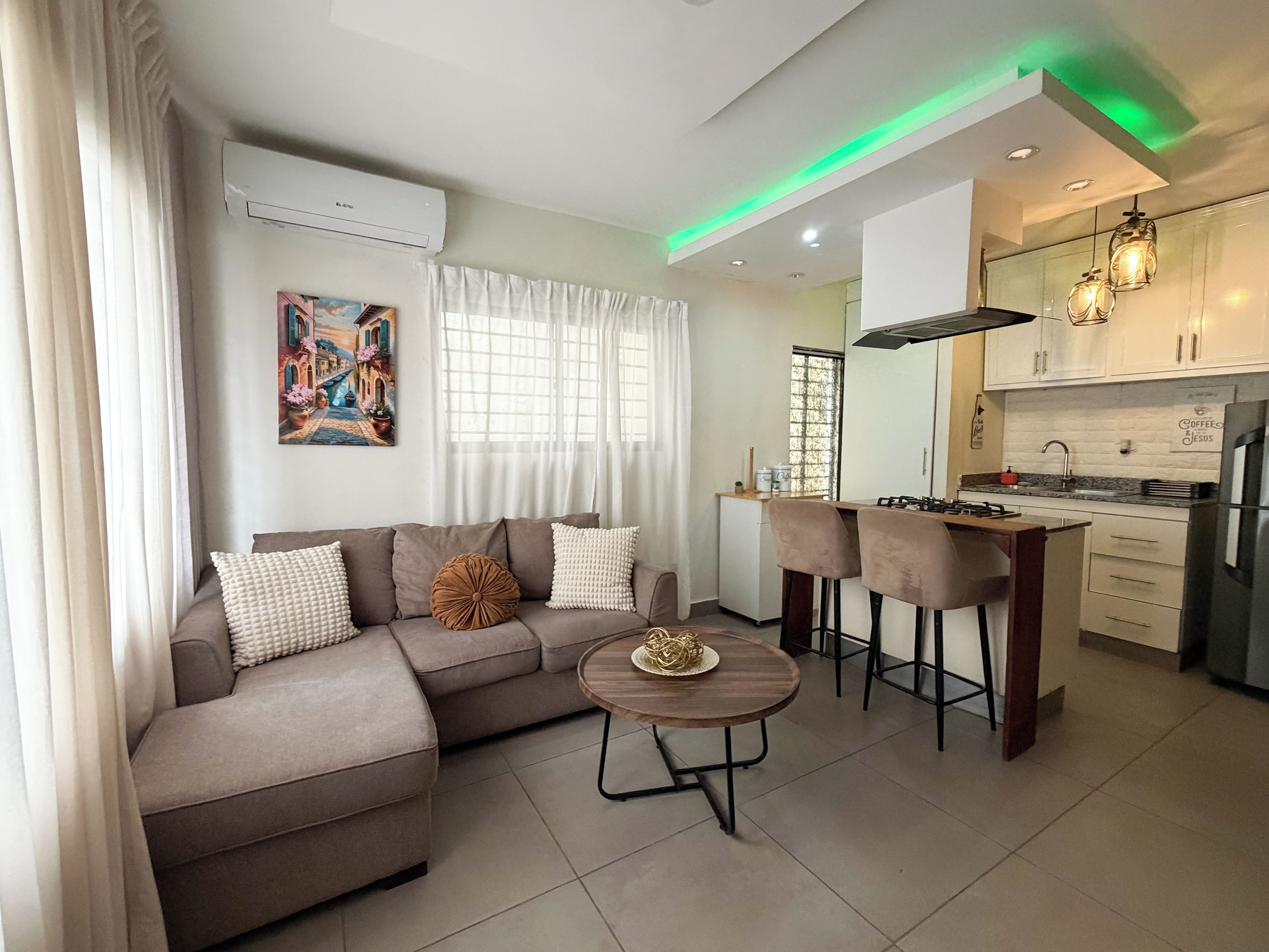 A modern living room with a sofa, a round coffee table, and a kitchen area with a gas stove and bar stools.