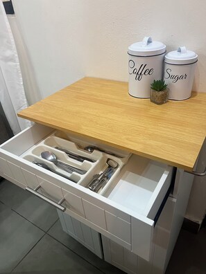Eine Schublade mit Küchenutensilien und zwei beschrifteten Behältern auf einer Holz Arbeitsplatte.