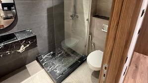 Een moderne badkamer met een douchecabine van glas, een marmeren wastafel en een houten deur.