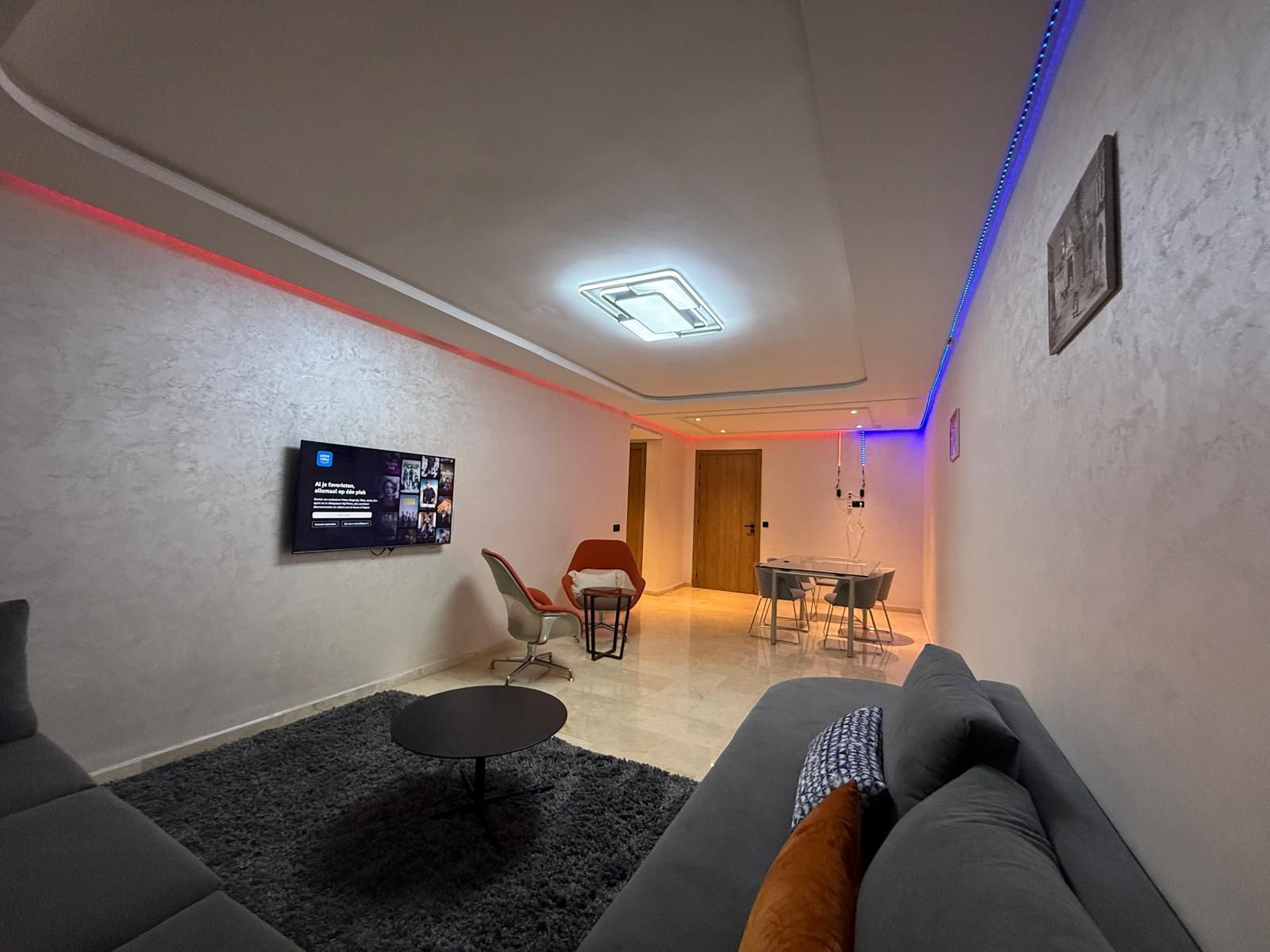 Un salon moderne avec un canapé, une petite table ronde et un téléviseur fixé au mur.