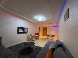Un salon moderne avec un canapé, une petite table ronde et un téléviseur fixé au mur.