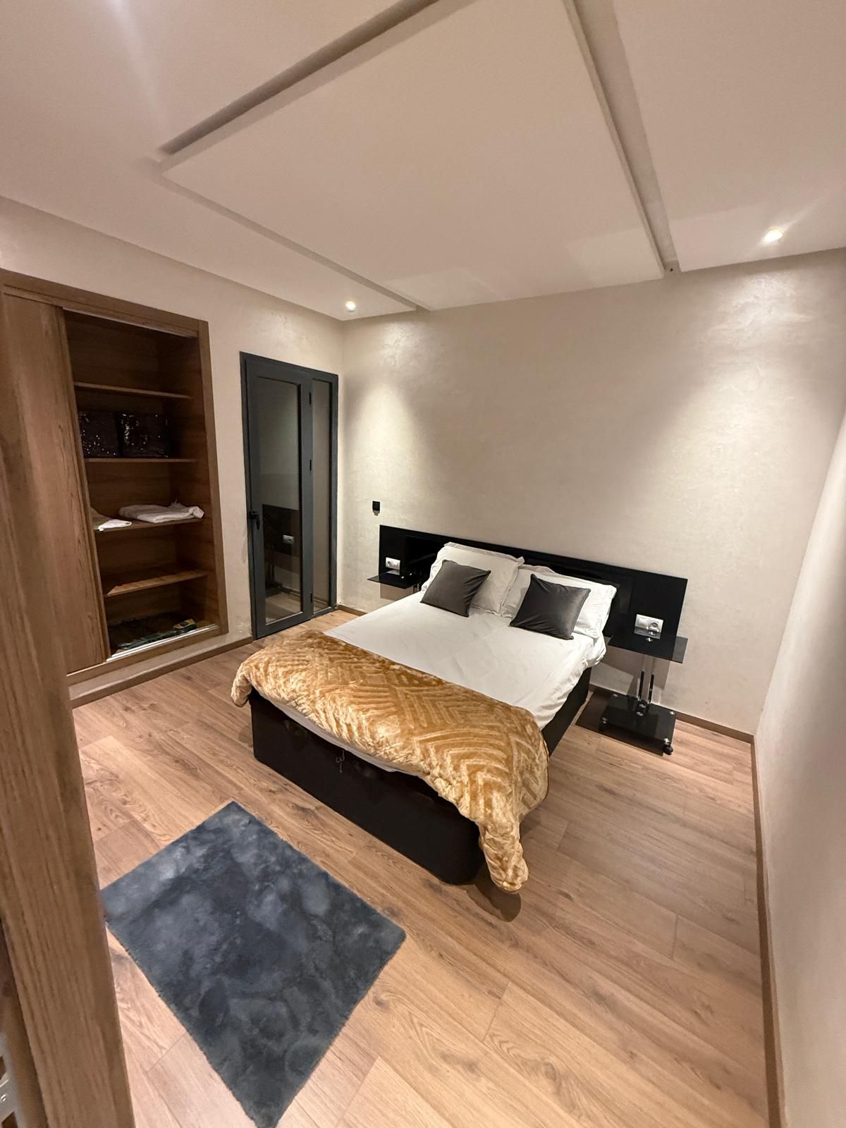 A modern bedroom with a bed, bedside tables, a wardrobe, and a door.