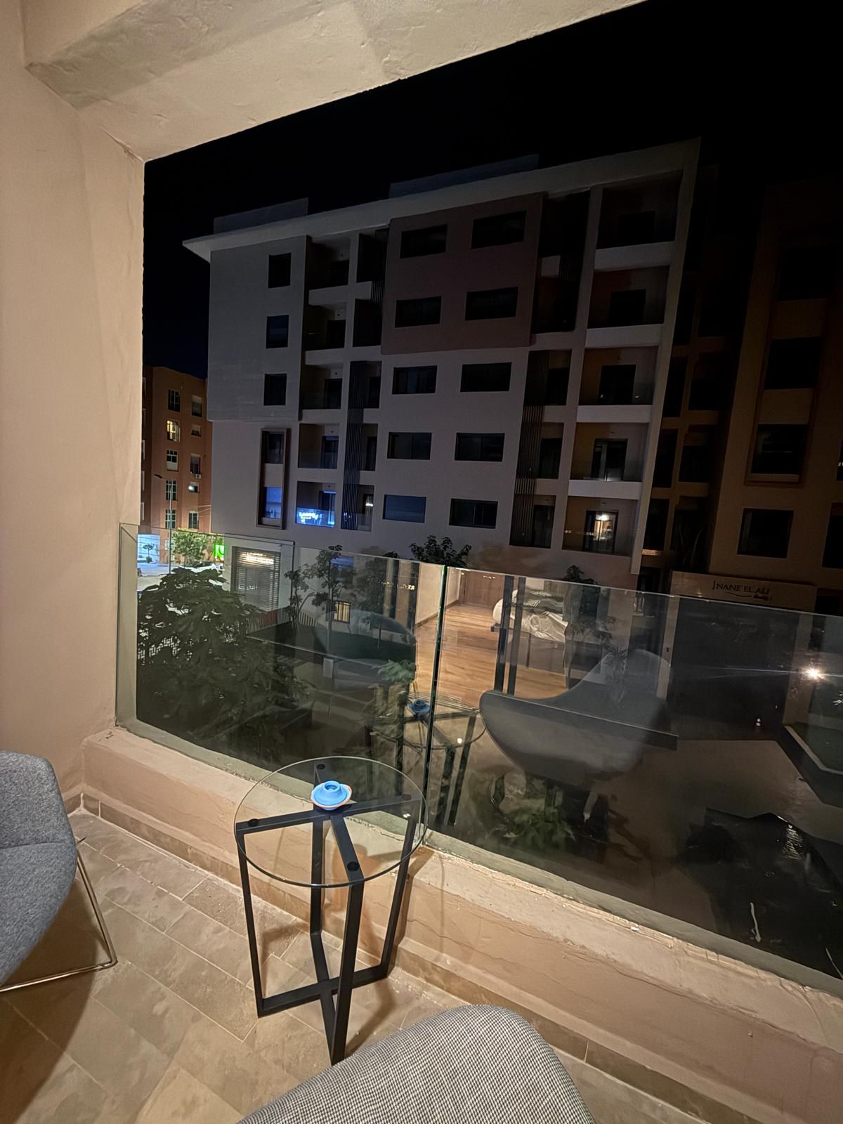 A balcony with a glass railing, a chair, and a small table.
